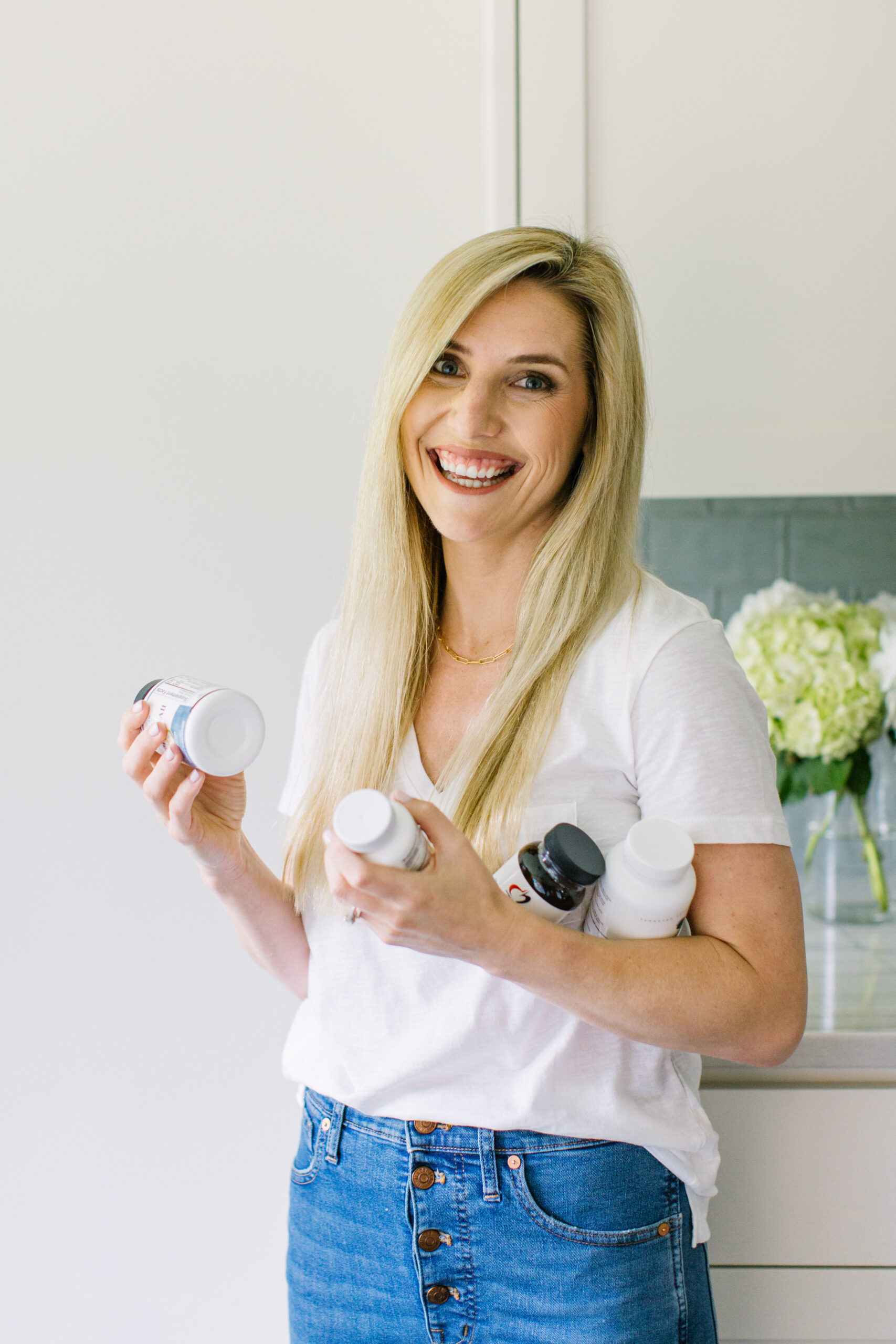 Taylor Dukes (white blonde woman wearing a white t-shirt and jeans) holding supplements